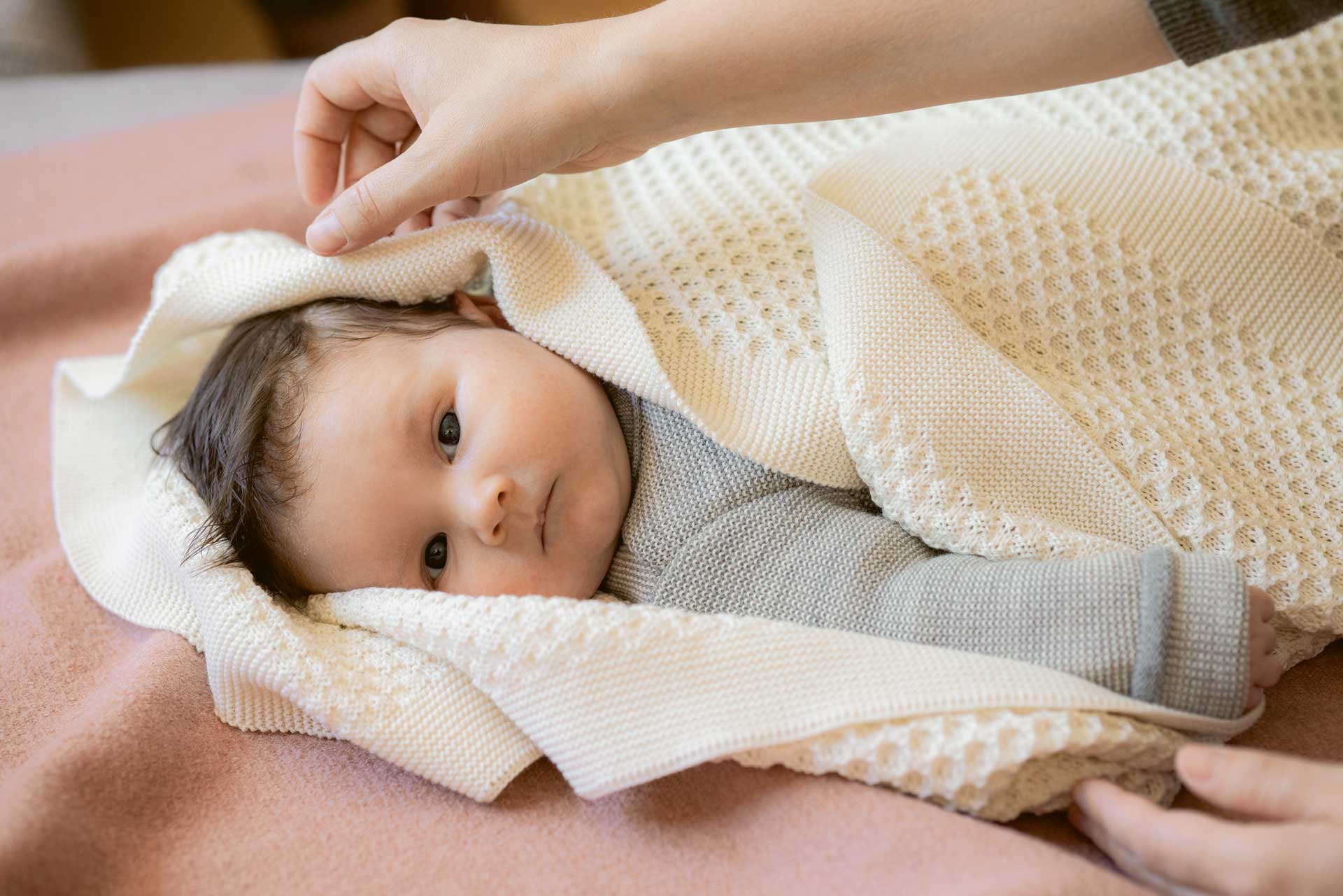 Baby wrapped in a cream organic merino wool knitted blanket