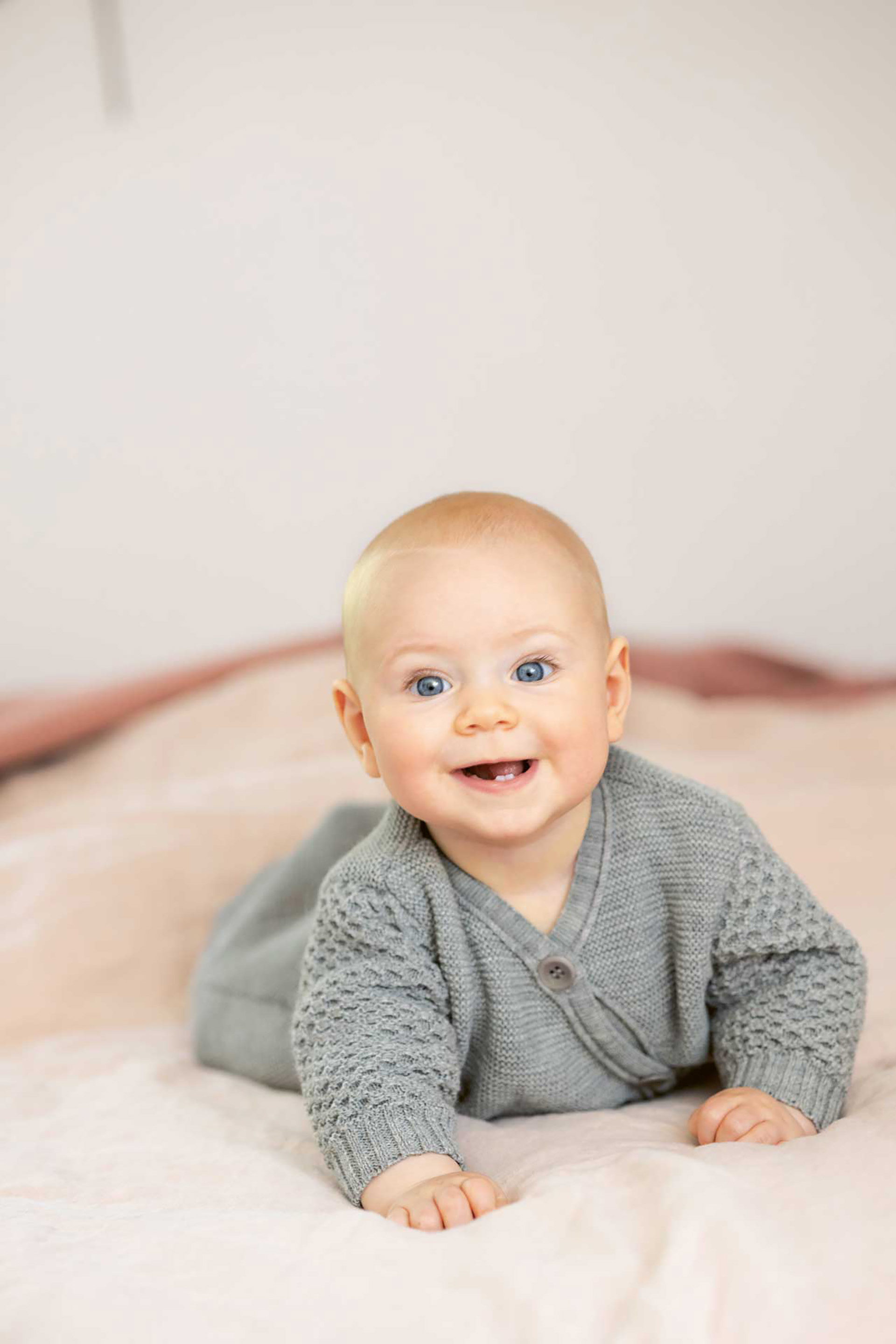 Baby mit großen blauen Augen im disana Langarm-Schlafsack in Grau auf dem Bauch auf Lammfell liegend
