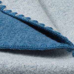 Nahaufnahme der disana Doubleface-Babydecke aus Bio-Merinowolle in Taubenblau-Natur mit typischer Muschelkante in Taubenblau