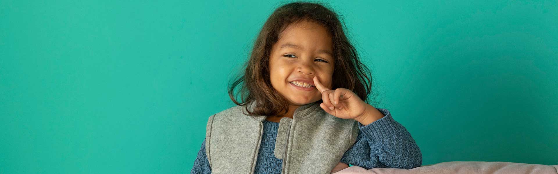 Smiling child in a wool vest against a turquoise background