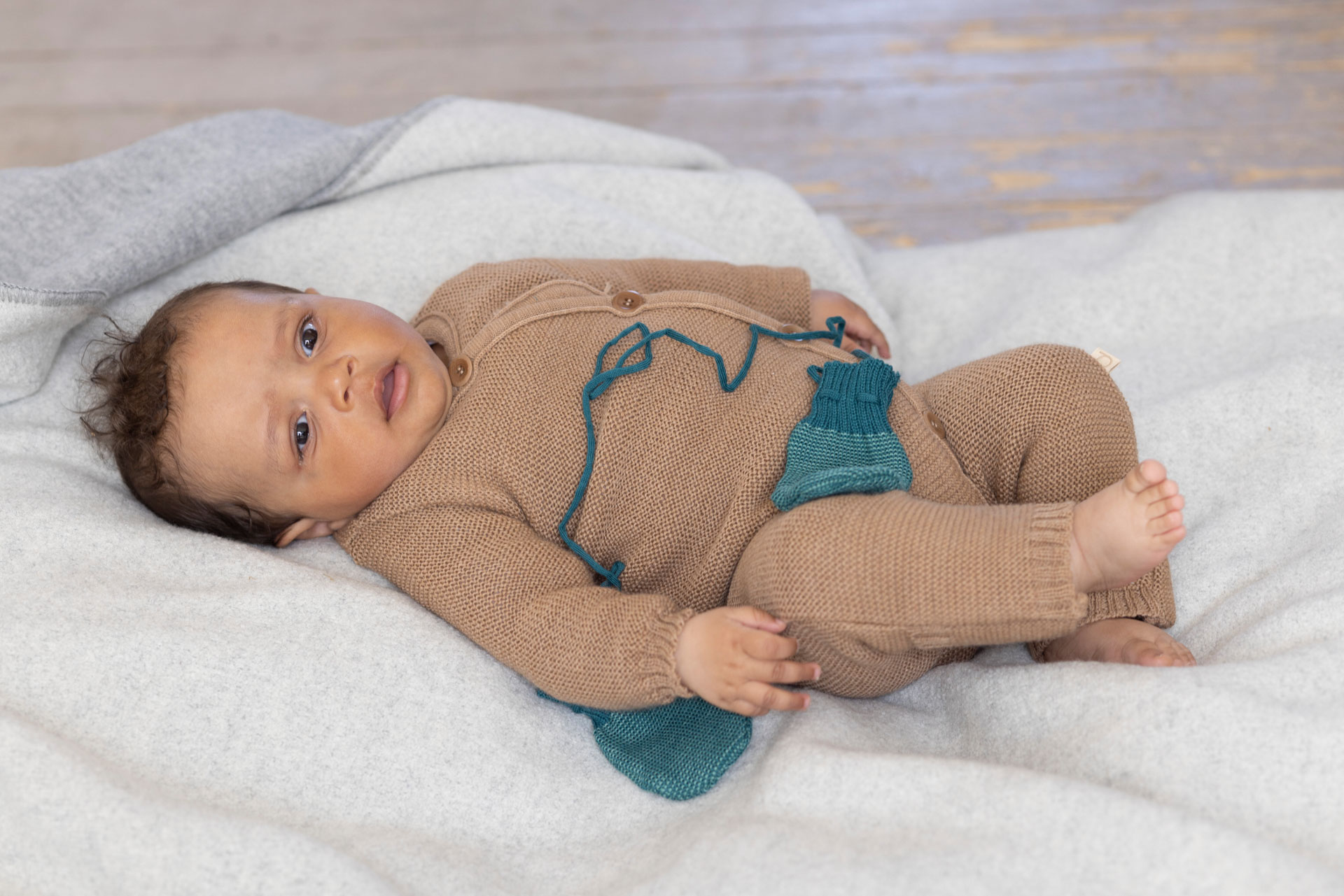 Baby in brown knitwear lying on a light wool blanket