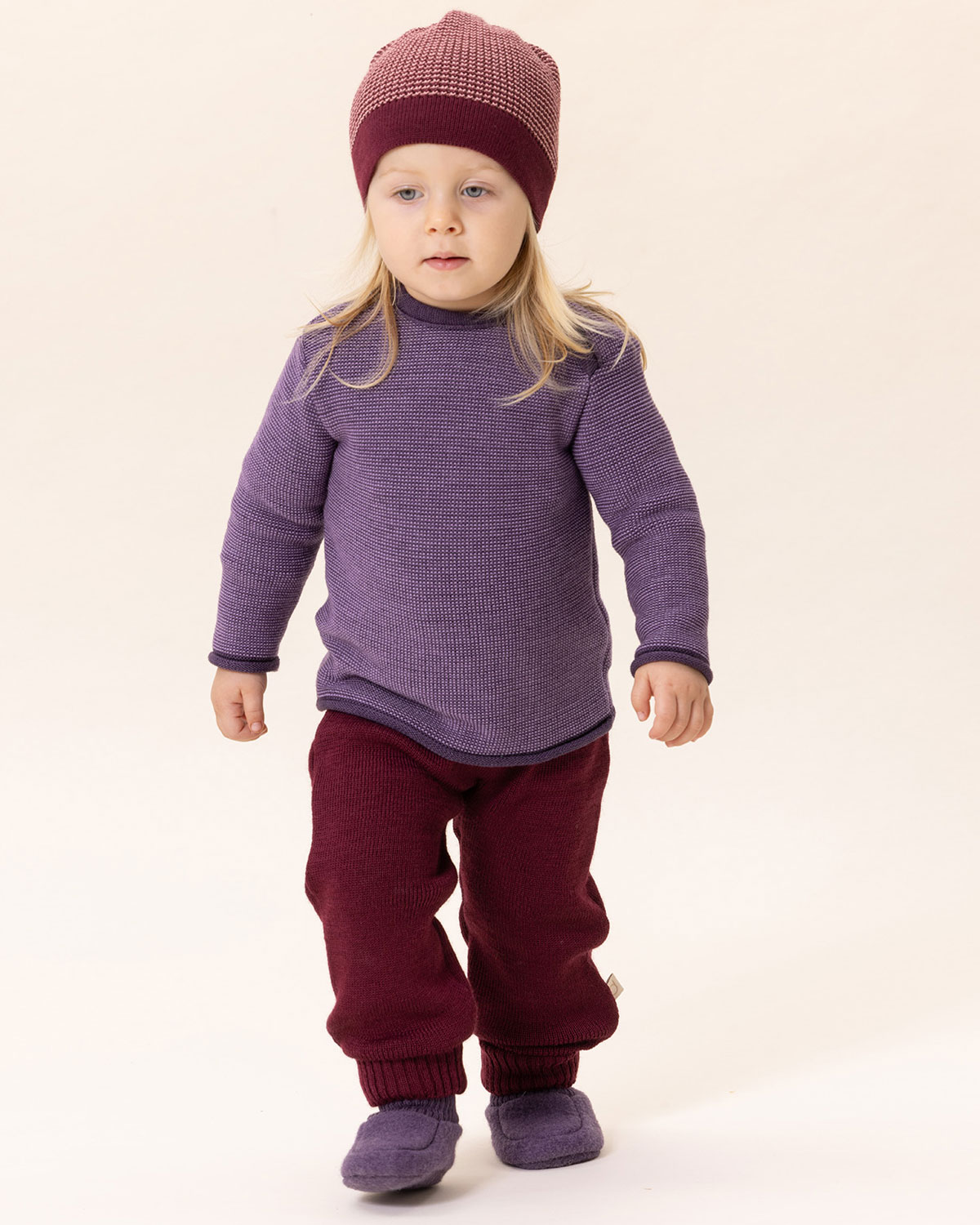 Child in a purple striped jumper, red boiled wool trousers and knitted hat