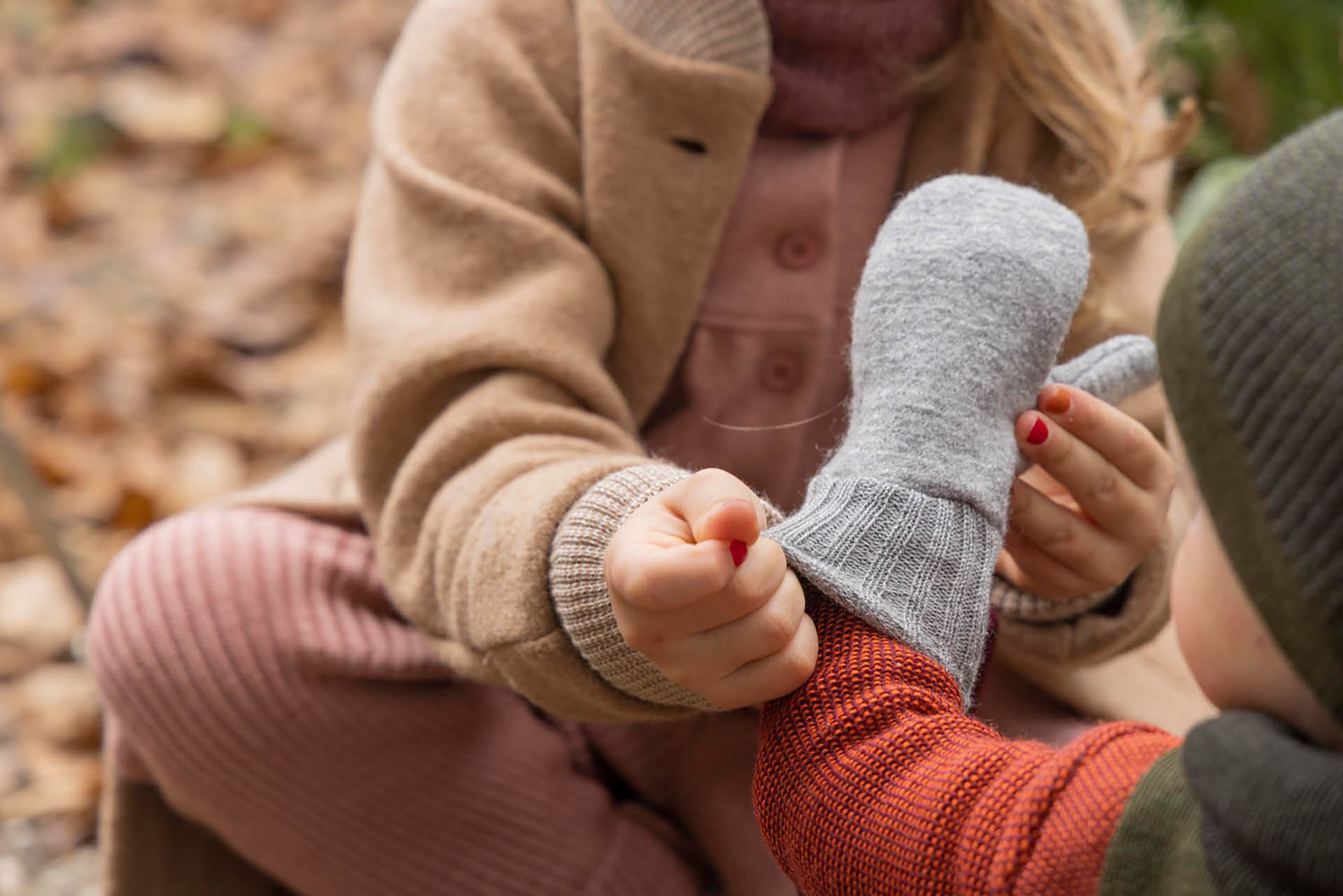 disana Kleinkind lässt sich eine disana Walk-Handschuhe in Grau von einem Mädchen mit disana Walk-Mantel Karamell anziehen
