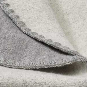 Nahaufnahme der disana Doubleface-Babydecke aus Bio-Merinowolle in Grau-Natur mit typischer Muschelkante in Grau