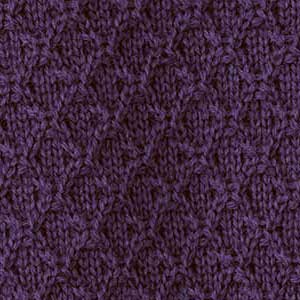 Nahaufnahme eines disana Strickstoffs aus Bio-Merinowolle in der Farbe Aubergine mit charakteristischem Aran-Muster